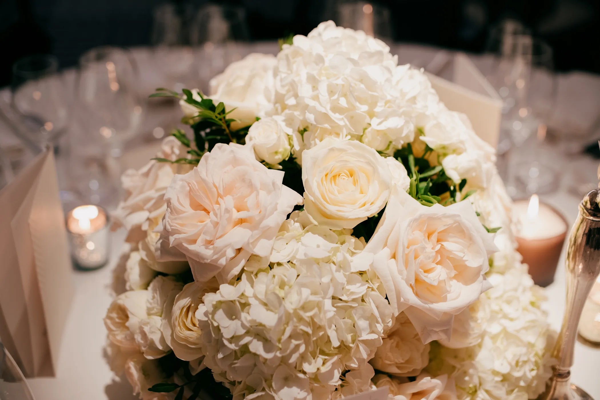 Bouquet of white and light pink flowers on a table with candles and silverware.