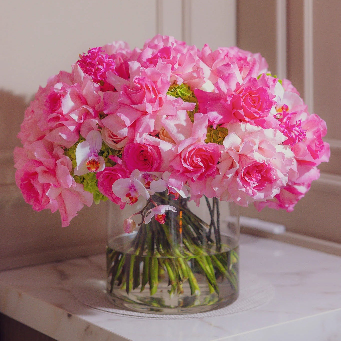Bouquet of pink and white flowers in a clear vase on a marble countertop.