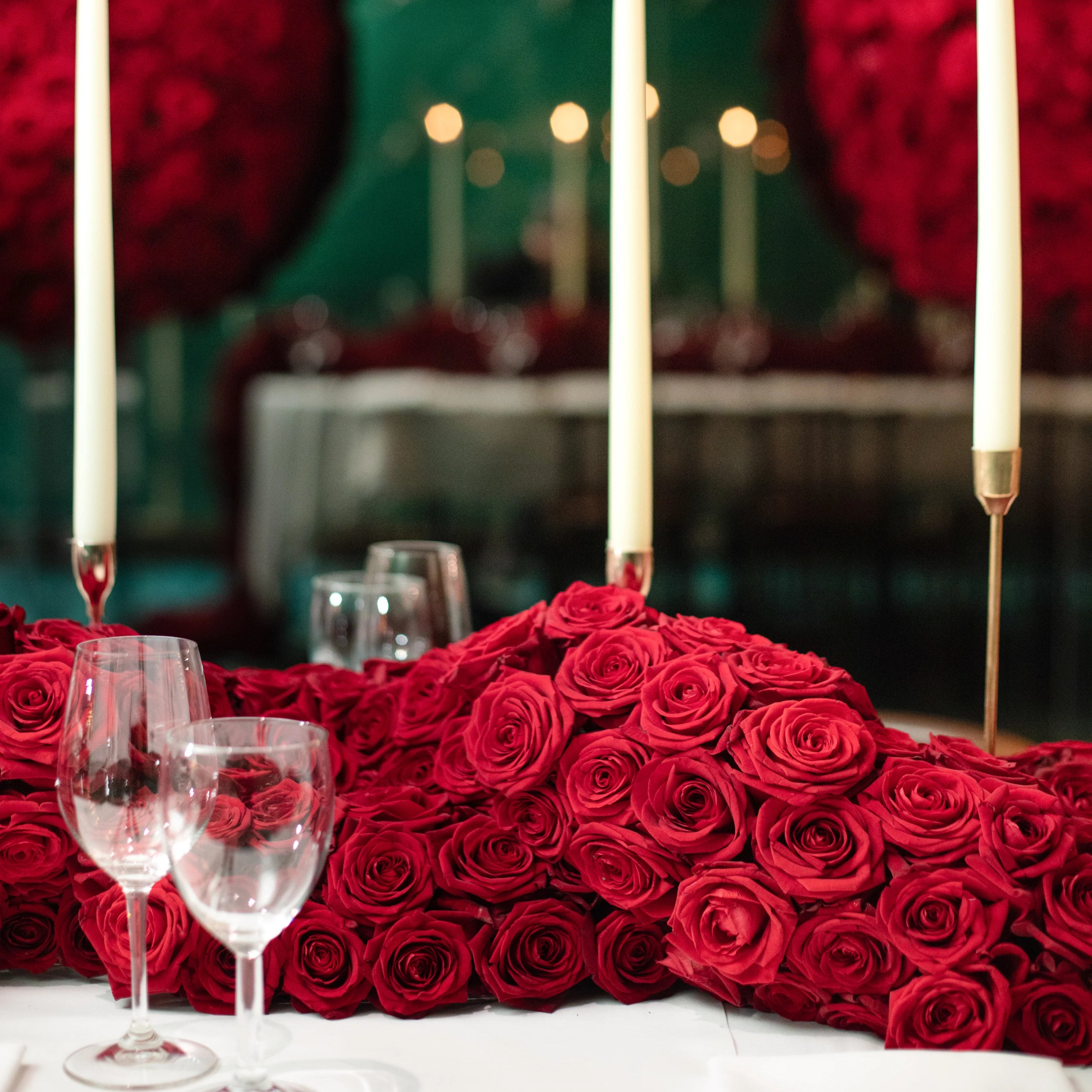 Decorative table setting with red roses, candles, and wine glasses.