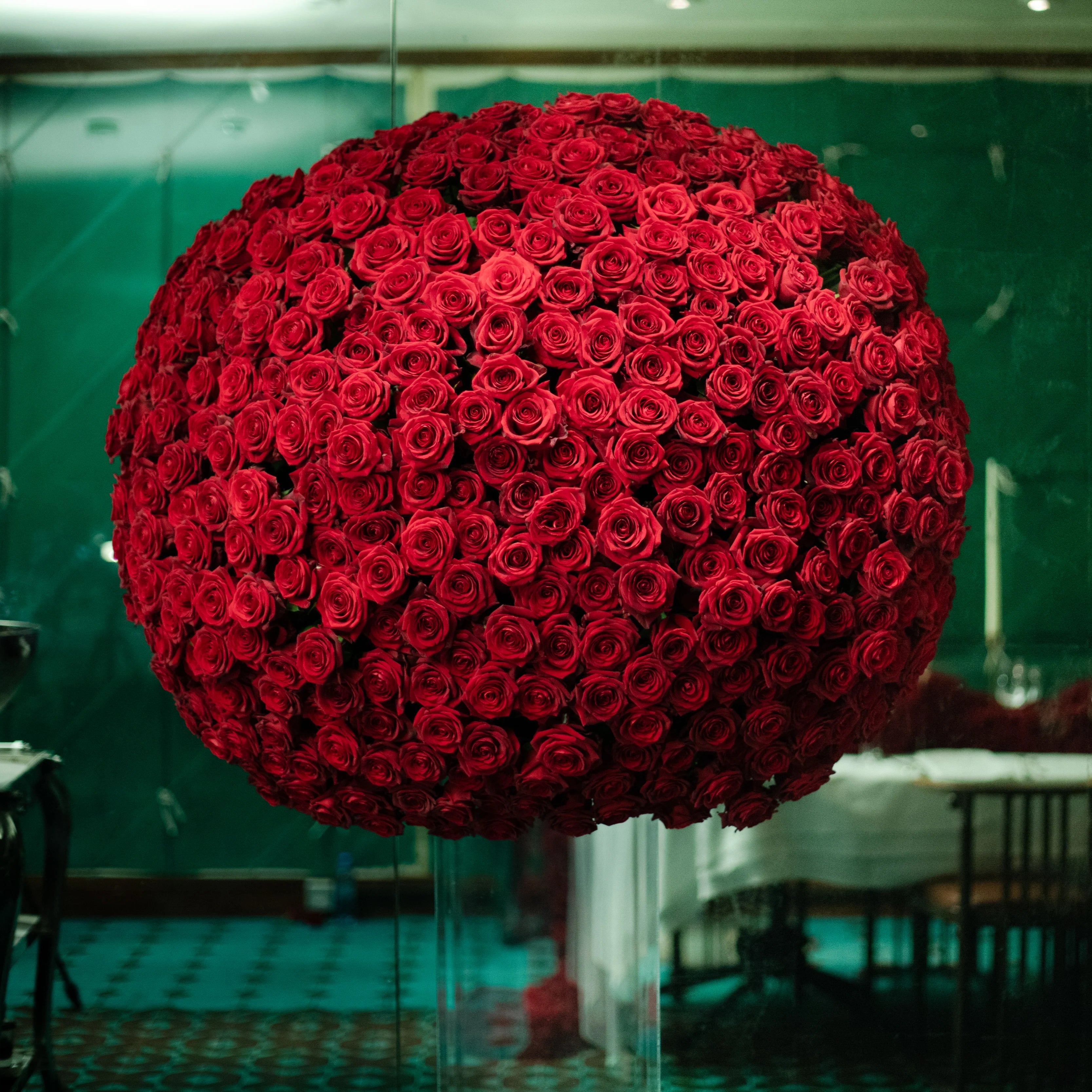 Large spherical arrangement of red roses in a room with tables and chairs.