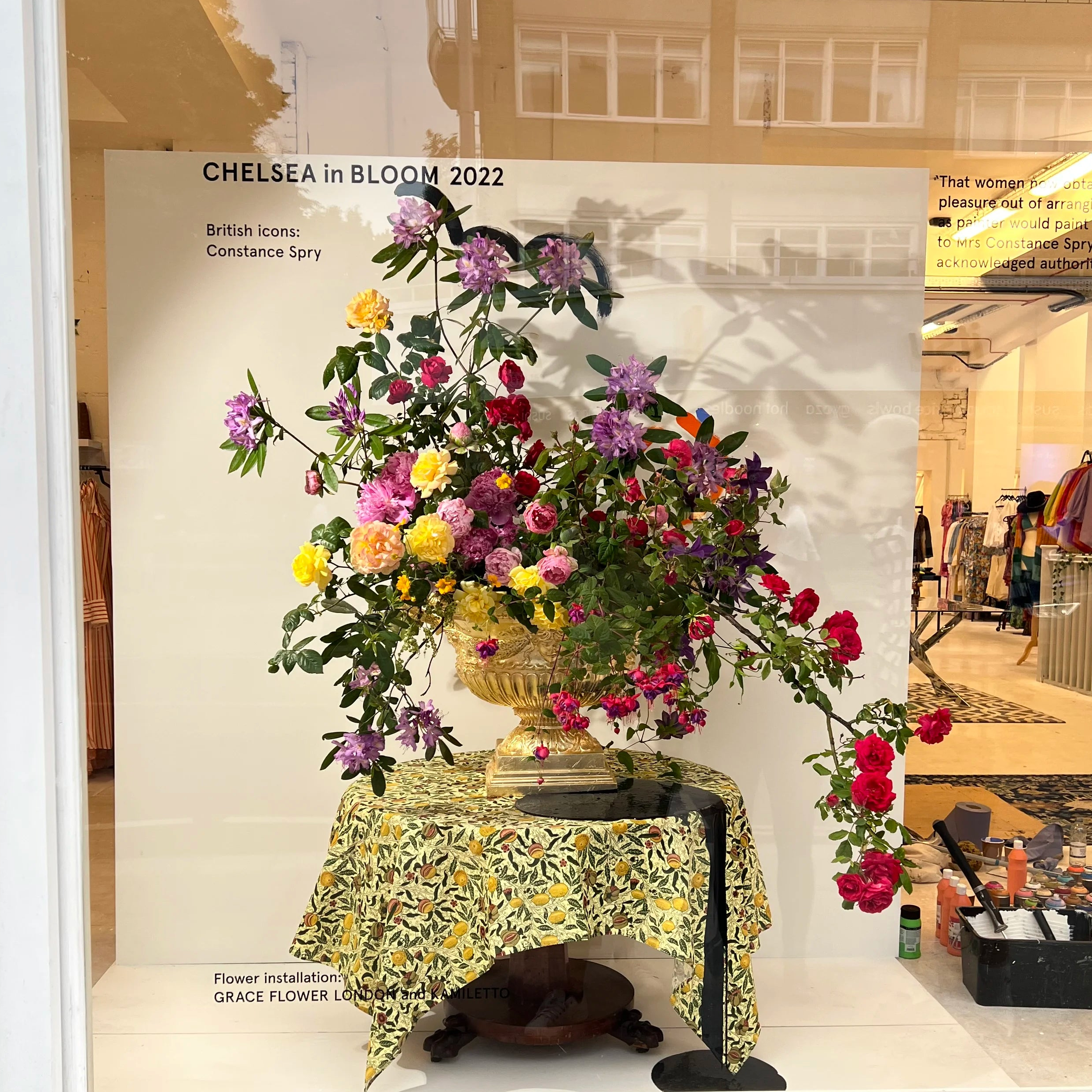 Floral installation in a store window with 'Chelsea in Bloom 2022' text.