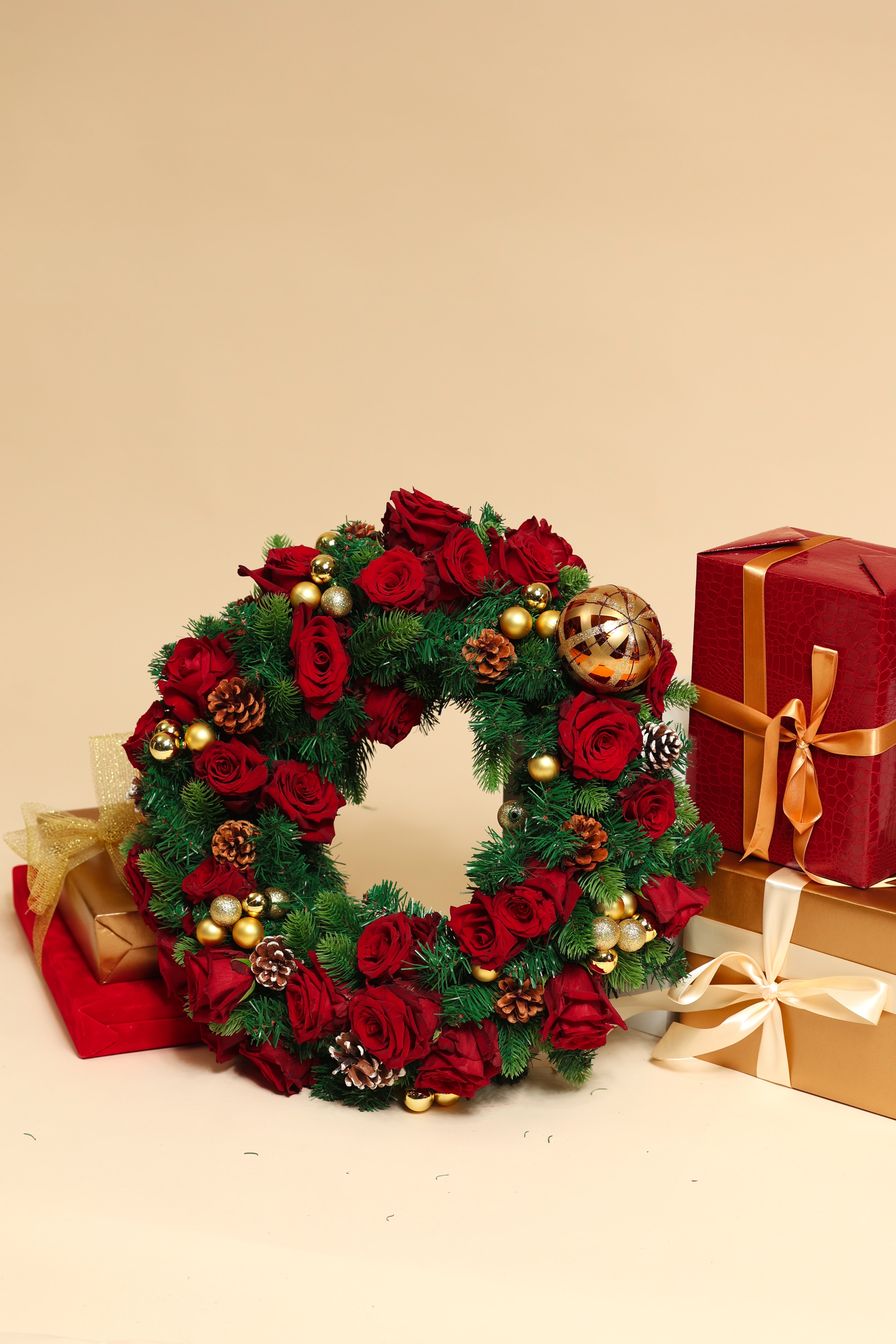 Decorative Christmas wreath with red flowers and gold ornaments on a beige background with presents.