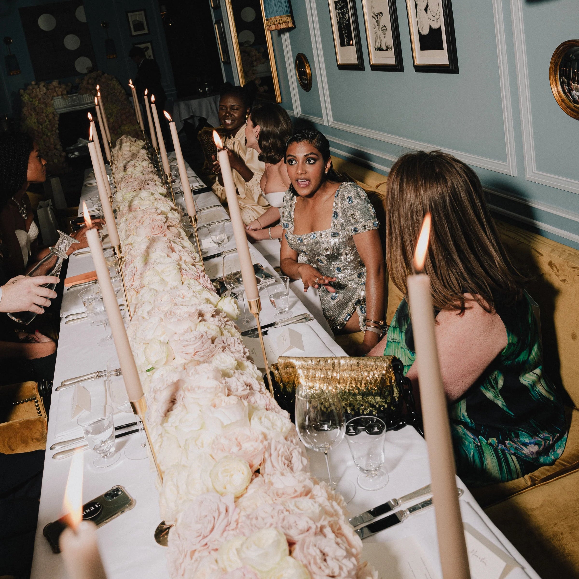 Dinner party scene with guests seated at a long table with decorative candles and tableware.