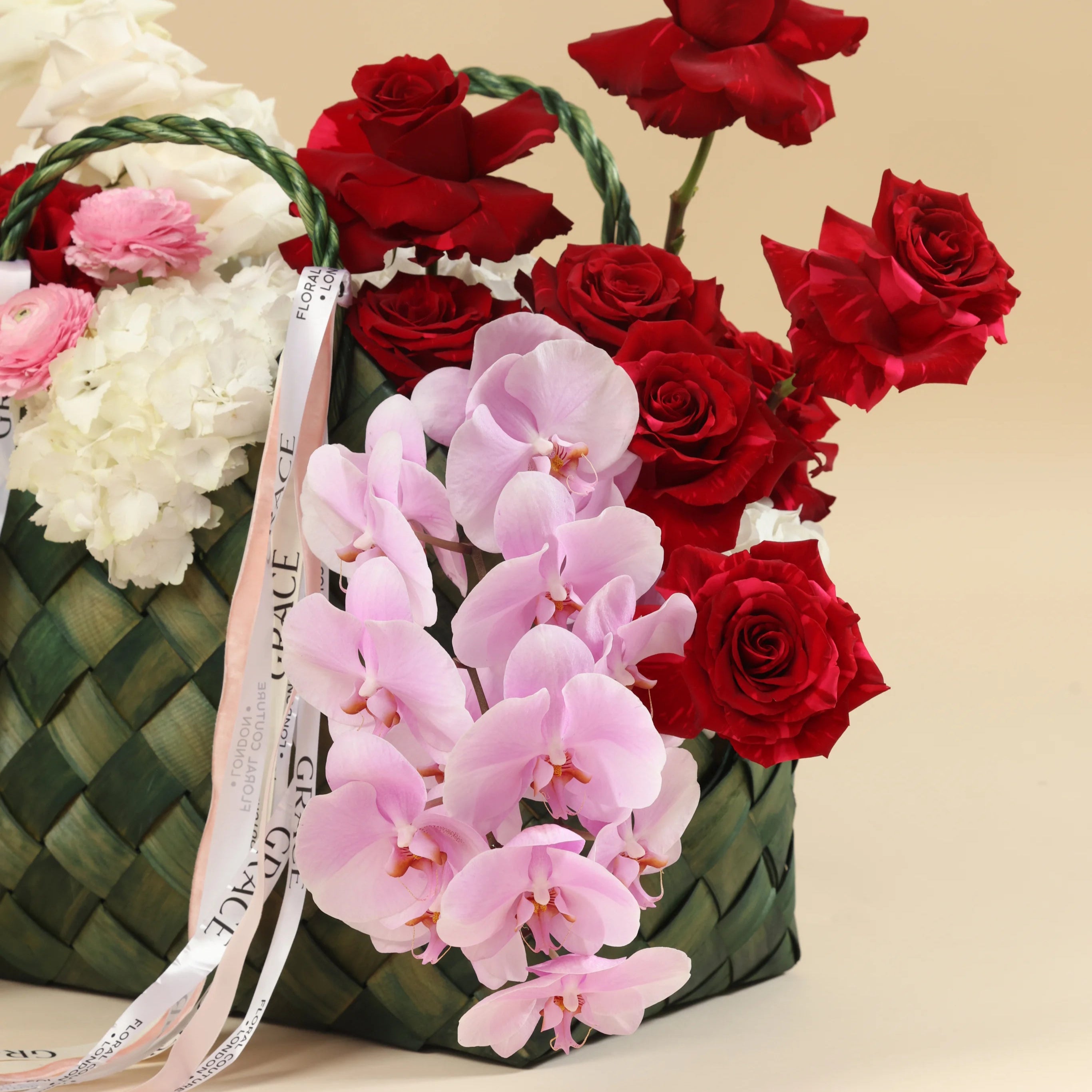 Floral arrangement with red roses and pink orchids in a woven basket on a beige background