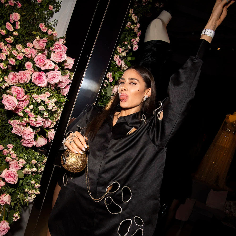 Woman in a black dress posing with a large black object against a floral background